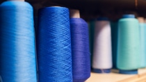 Background with a lot of blue coils with threads. Bobbins are stacked in a rows, one on the other. Selective focus. Background with a lot of blue coils with threads. Bobbins are stacked in a rows, one on the other. Selective focus.